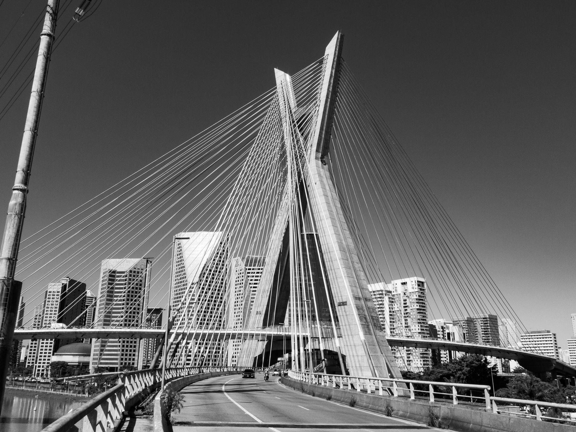 Black and white photo of a modern cable-stayed bridge with city skyscrapers in the background.